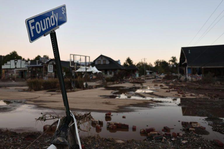 Flooded street scene with a bent street sign, debris, and damaged buildings in the background.